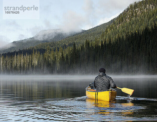 Rückansicht eines Mannes  der mit einem Boot auf einem ruhigen  nebligen See in Kanada paddelt