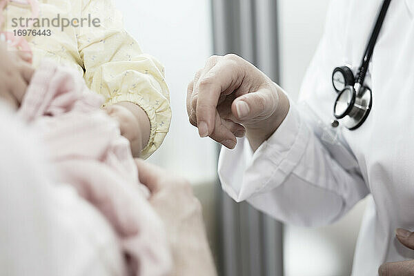 eine junge Ärztin hält ihre Hand an ein Kind in den Armen seiner Mutter