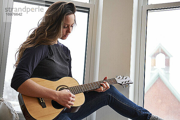 Junge Musikerin spielt Gitarre am Morgen