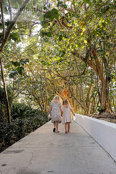 zwei Mädchen gehen händchenhaltend auf einem Weg durch Bäume