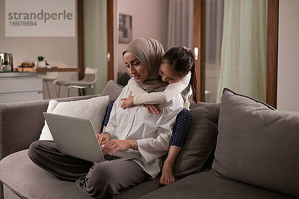 Muslimische Mutter mit Tochter bei der Arbeit auf der Couch