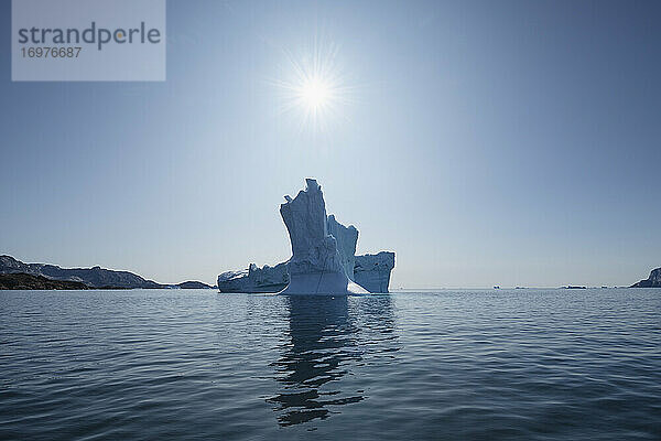 Die Sonne scheint am blauen Himmel über einem Eisberg  Sermilik Fjord  Ostgrönland