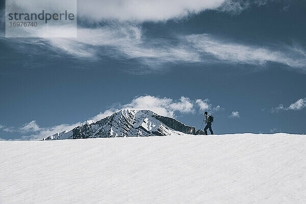 Junger Mann starrt auf einen schneebedeckten Berg  während er über einen verschneiten Bergrücken wandert