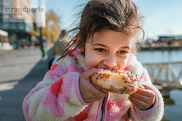 Junges Mädchen isst Donut mit Streuseln im Freien