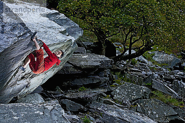 Frau beim Bouldern am Felsen im Schiefersteinbruch in Nordwales