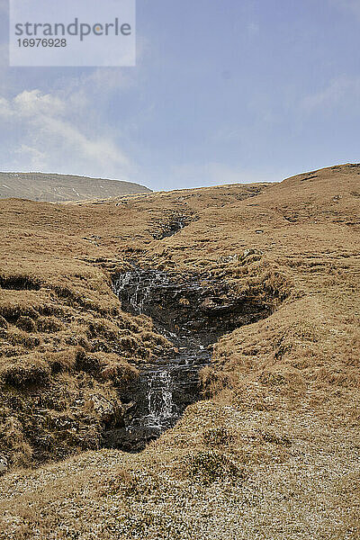 Bach entlang eines Hügels auf den Färöer Inseln