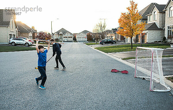 Zwei Jungen spielen Streethockey in einer Wohnstraße im Herbst.