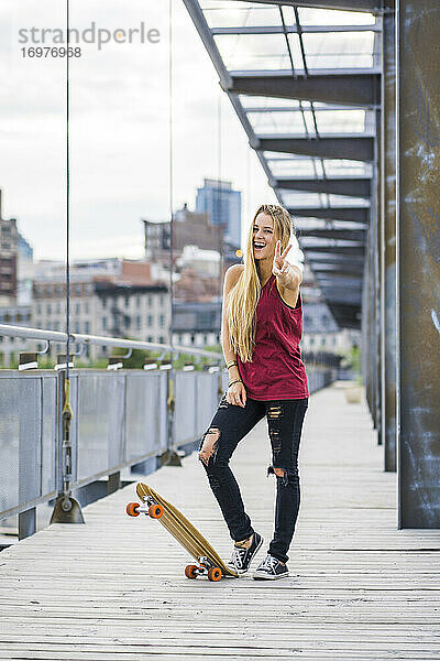 Weibliche Skateboarderin mit einem Friedenszeichen und lächelnd downtow