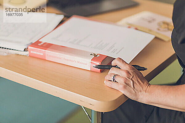 Lehrerin ordnet Notizen auf dem Schreibtisch  Fokus auf Hand und schwarzem Stift.