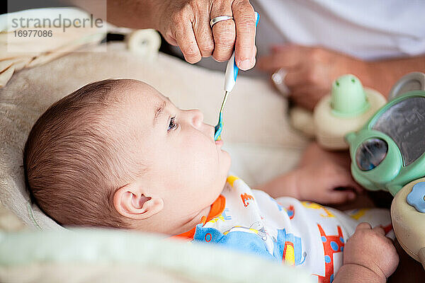 Das Baby erhält seine erste feste Mahlzeit mit einem blauen Löffel.
