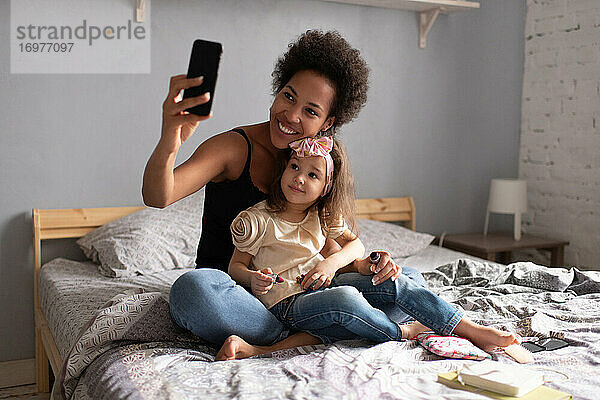 Fröhliche ethnische Mutter mit Tochter  die einen Videoanruf auf dem Smartphone macht