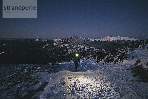 Mann mit Schneeschuhen und Stirnlampe beim Wandern vor Sonnenaufgang vor schneebedeckten Berggipfeln  Guadarrama  Madrid