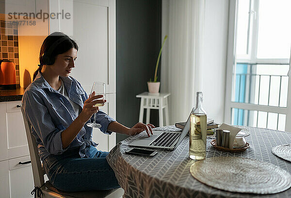 Frau mit einem Glas Wein und einem Laptop genießt die freie Zeit zu Hause