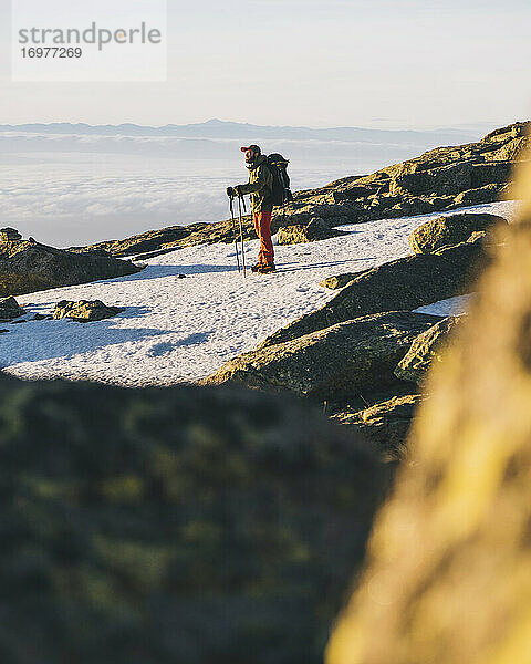 Junger Mann mit Mütze und Blick auf die über dem Horizont aufgehende Sonne  Gredos  Spanien