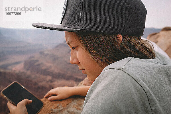 Junge prüft sein Telefon über einem Canyon Overlook