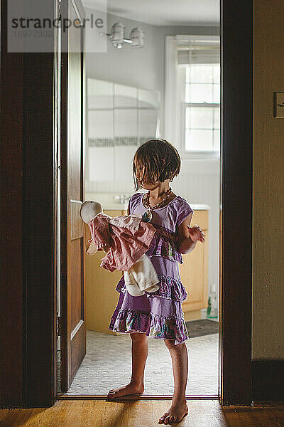 Ein barfüßiges Kind steht allein in der Tür und hält ein Stofftier