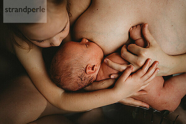 Draufsicht auf ein neugeborenes Baby  das gestillt wird  und eine ältere Schwester  die es umarmt