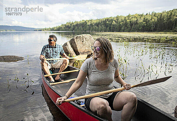 Lächelndes erwachsenes Paar paddelt in einem roten Kanu zwischen Seerosenblättern auf einem See