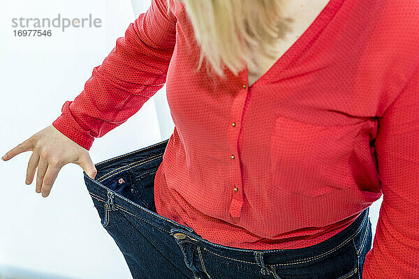 eine junge Frau zeigt den Erfolg ihrer Gewichtsabnahme mit angezogener Hose