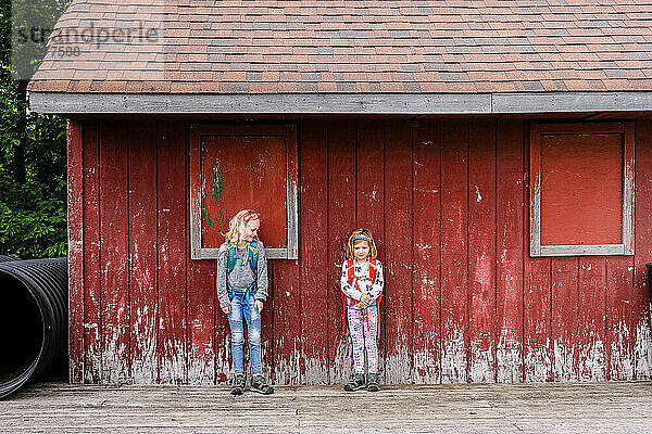 zwei Mädchen stehen zusammen vor einer verwitterten roten Scheunenwand