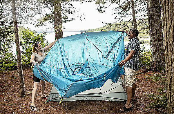 Ehepaar stellt blaues Zelt in der Nähe eines Sees beim Camping im Wald in Maine auf
