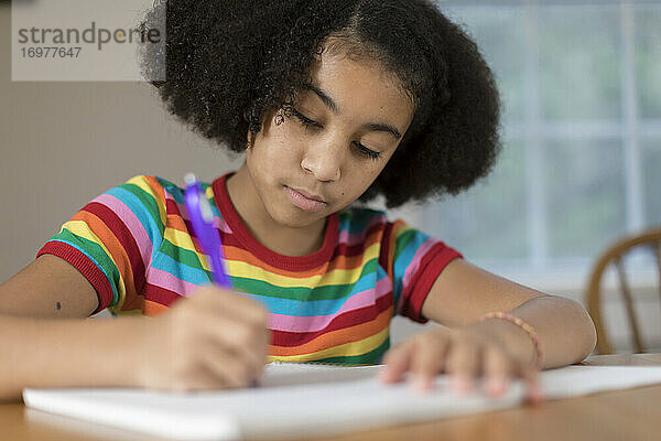 Zehnjähriges gemischtrassiges Mädchen macht am Tisch Hausaufgaben