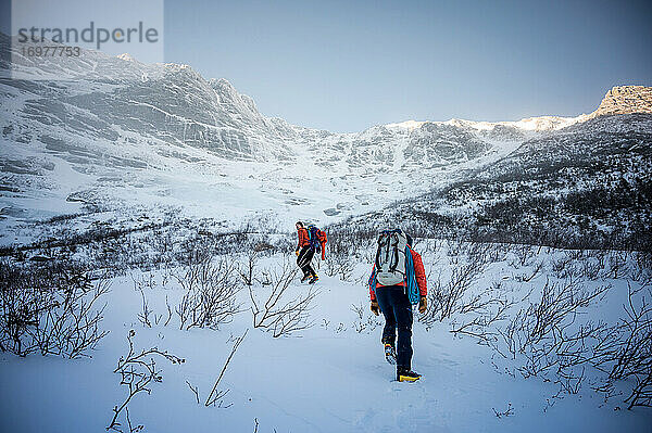 Zwei männliche Bergsteiger gehen im Winter auf einen Bergkamm zu