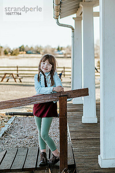 Glückliches junges Mädchen steht auf der Terrasse und lächelt an einem sonnigen Tag