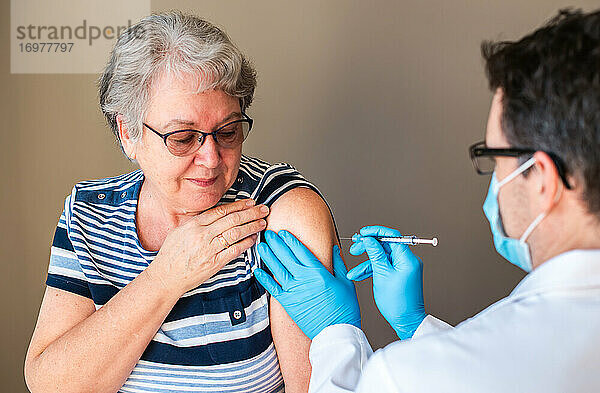 Ältere Frau  der ein Arzt einen Impfstoff in den Oberarm spritzt.