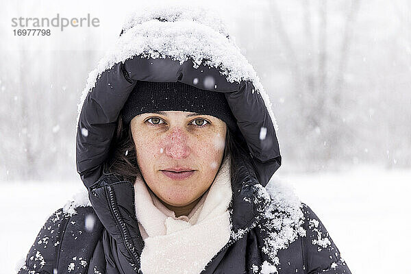 Ruhige Frau in warmer Oberbekleidung  bedeckt mit Schnee  im Winter im Wald stehend  während sie einen Spaziergang macht