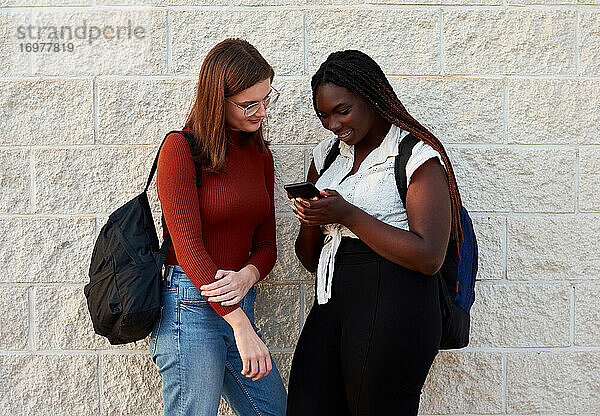 Zwei junge Frauen schauen auf ihr Smartphone. Multiethnisches Konzept