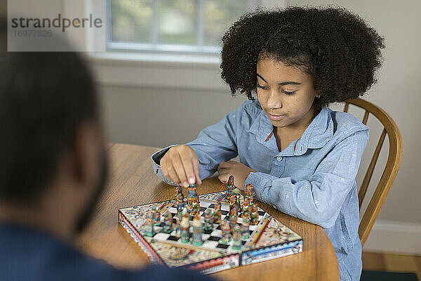 Ein zehnjähriges afroamerikanisches Mädchen spielt mit seinem Vater ein Brettspiel