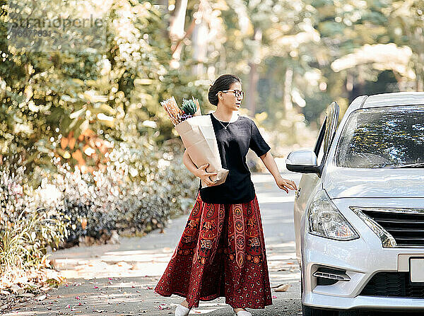 Eine Frau hält eine Papiertüte mit Trockenblumen und geht nach dem Einkaufen zurück zum Auto