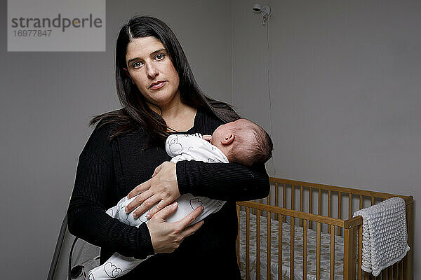 Ruhige Frau  die ein winziges Neugeborenes umarmt  während sie im Kinderzimmer steht