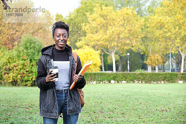 Universität afrikanische Studentin mit Rucksack  Ordner und eine Tasse Kaffee draußen auf dem Campus. College-Leben-Konzept.