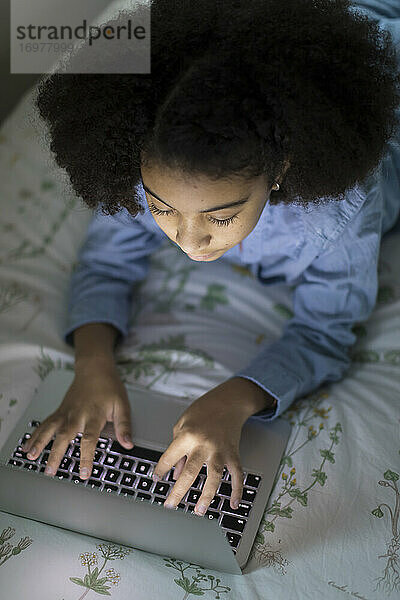 Draufsicht auf ein zehnjähriges gemischtrassiges Mädchen bei der Arbeit am Laptop