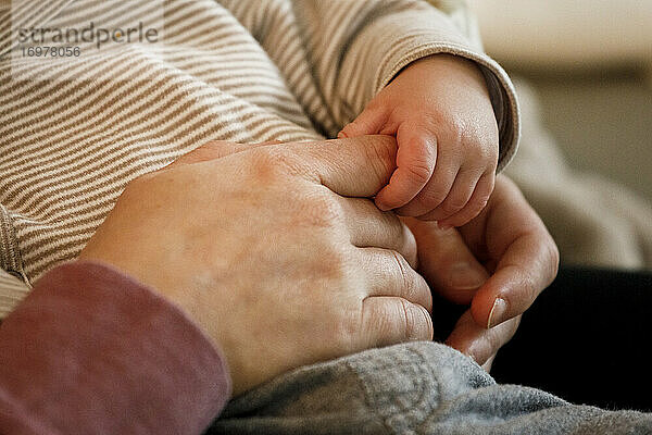 Ein 2 Monate altes Baby hält den Finger seiner Mutter mit seiner kleinen Hand