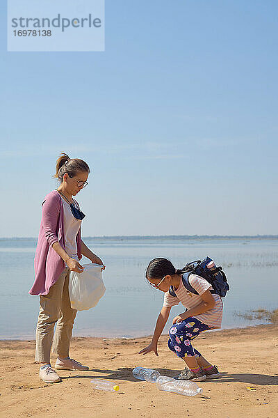 Tochter und Mutter sammeln gemeinsam Plastikflaschen am See