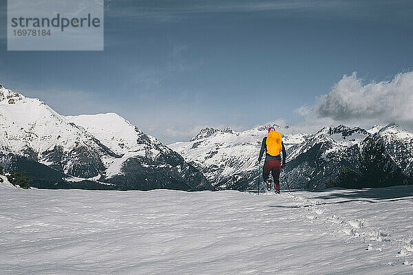 Junger Mann geht im Tiefschnee gegen schneebedeckte Berge
