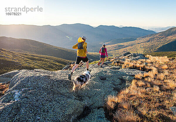 Mann und Frau beim Trailrunning mit Hund in den Bergen bei Sonnenaufgang