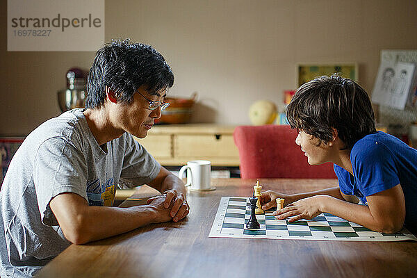 Ein Junge macht einen Schachzug  während er mit seinem Vater am Esszimmertisch spielt