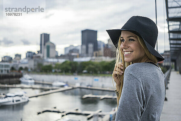 Blonde Frau mit Hut und Stadtsilhouette im Hintergrund