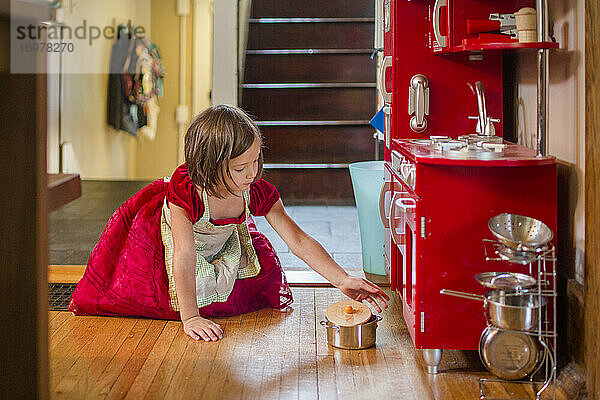 kleines Mädchen in Schürze und Partykleid spielt mit Spielzeugküche