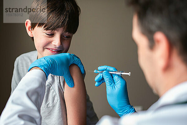 Nervös aussehendes Kind  das von einem Arzt geimpft wird  der eine Nadel hält.