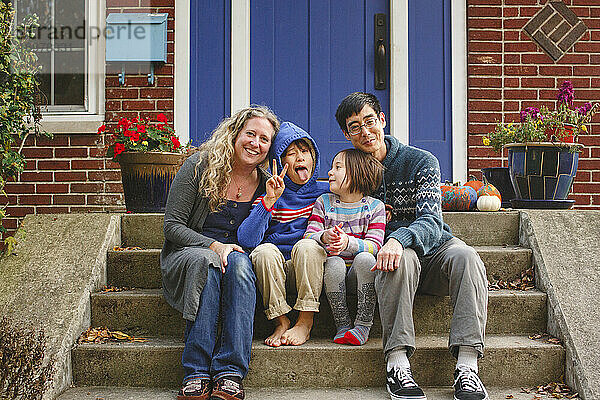 Eine glückliche Familie sitzt lächelnd auf der Treppe vor ihrem Haus zusammen
