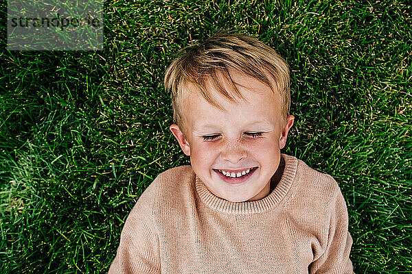 Lächelnder Junge  der draußen im Gras liegt