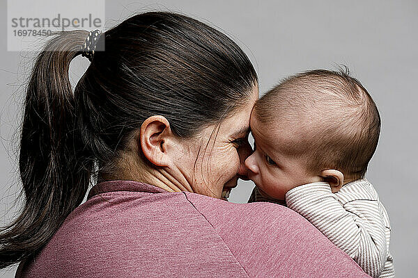 Eine Mutter hält ihr neugeborenes Baby im Arm und betrachtet es liebevoll und lächelnd