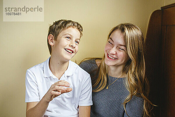 Zwei Geschwister sitzen zusammen auf einer Holzbank und lachen vor Freude im Haus