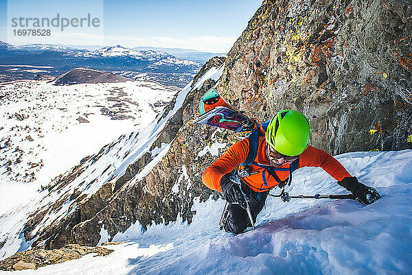 Mann mit Splitboard auf dem Rücken erklimmt steile Schneerinne