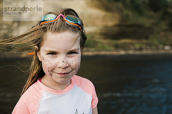 Lächelndes Mädchen am Wasser  das Rashie und Schutzbrille trägt